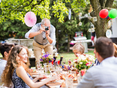 Family celebration outside in the backyard. Big garden party. Grandfather taking photo with a camera.